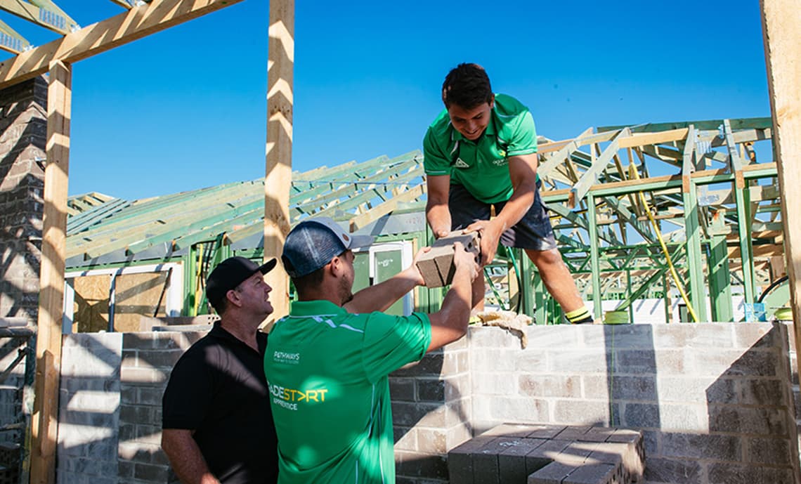 A bricklaying apprentice being handed bricks