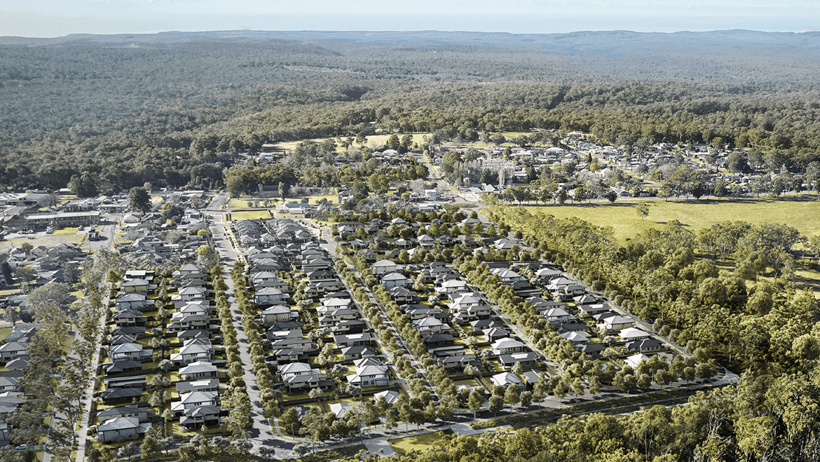 Aerial view of a suburban residential area with rows of houses surrounded by trees, bordered by a forest and open fields under a bright sky.
