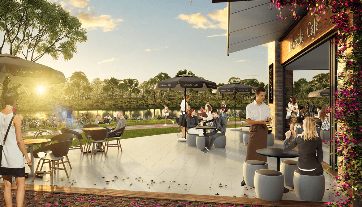 People dine at an outdoor lakeside café at sunset. Some sit at tables under umbrellas, while a waiter serves a customer. Trees, water, and greenery create a serene background. The scene feels relaxed and social.