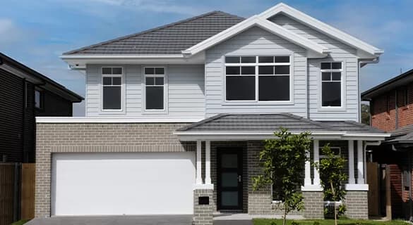 A modern two-story house with light gray siding, brick detailing on the lower level, large windows, a dark gray tile roof, a double garage, and a small front porch with two columns and young trees.