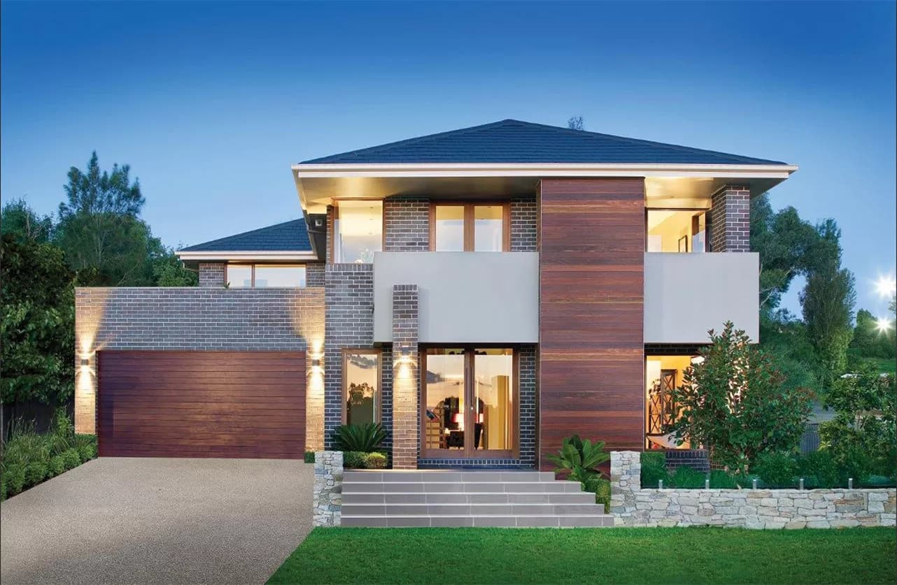 Modern two-story house with brick and wood panel exterior, large windows, double garage, wide front steps, landscaped garden, and green lawn under a clear blue sky.