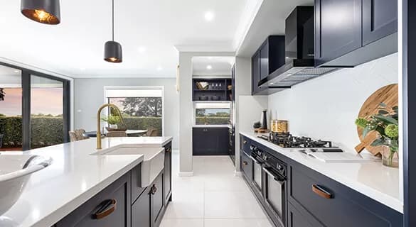 Modern kitchen with dark blue cabinets, white countertops, built-in appliances, gas stove, and pendant lights. Large windows and sliding doors offer views of greenery and outdoor seating area.