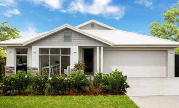 A modern single-story house with a white exterior, large front windows, a gray roof, and a double garage, surrounded by green shrubs and a well-maintained lawn under a blue sky.