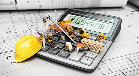 A large calculator on top of architectural blueprints is covered with miniature construction tools, equipment, a yellow hard hat, bricks, and wooden planks, symbolizing construction cost estimation.
