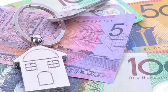 A house-shaped keychain rests on Australian banknotes, including $5, $50, and $100 bills, symbolizing real estate and finance.