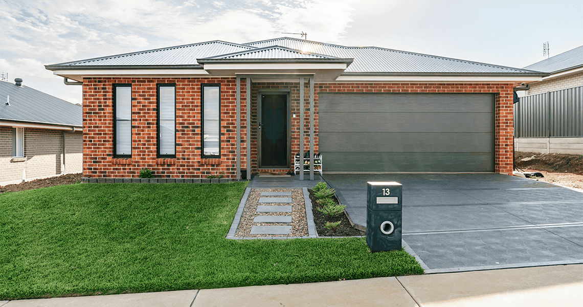 A modern single-story brick house with a grey metal roof, a double garage, narrow vertical windows, a front path with stepping stones, green lawn, and a mailbox labeled 13.